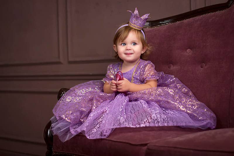 adorable baby girl dressed up as a princess sitting on the couch