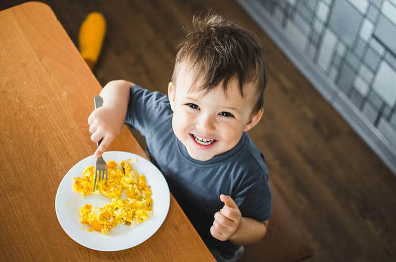 adorable little boy smiling while eating scrambled eggs