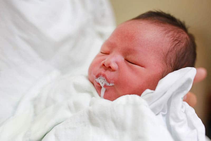 an infant baby in white clothes belching in mother's hands