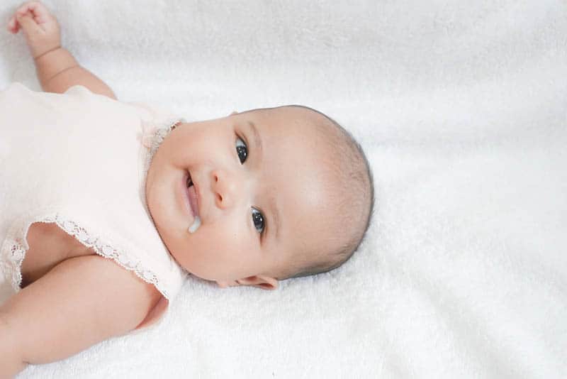 cute baby girl lying on bed and spitting up