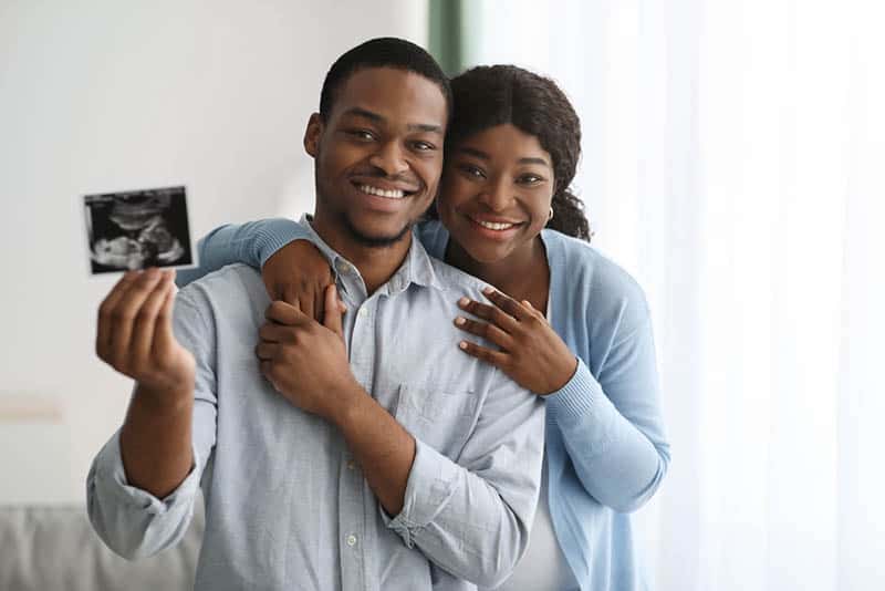 happy pregnant woman and husband holding sonogram in hand