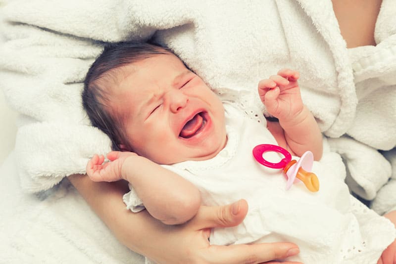 newborn baby crying on the bed next to mother