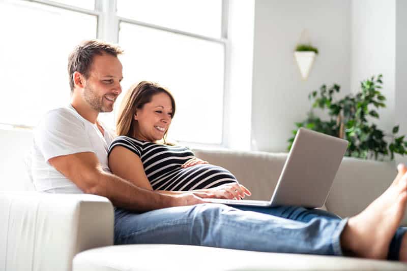 pregnant woman and husband lying on the couch and looking at laptop