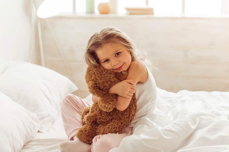 sweet little girl sitting on the bed and hugging a teddy bear