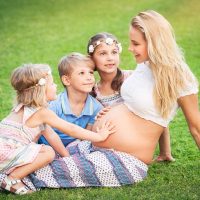 pregnant woman sitting with her three kids on the grass