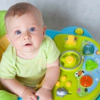 baby sitting in a green baby walker on the carpet