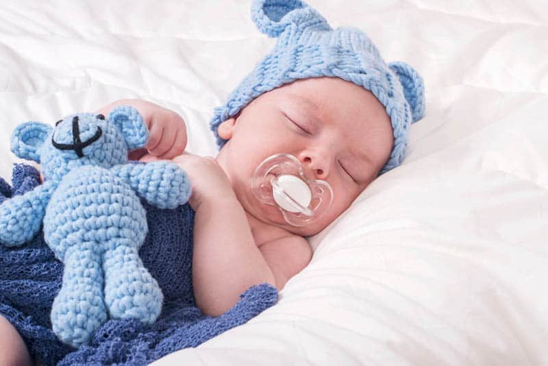 cute baby with winter hat and a pacifier sleeping in bed with his bunny toy