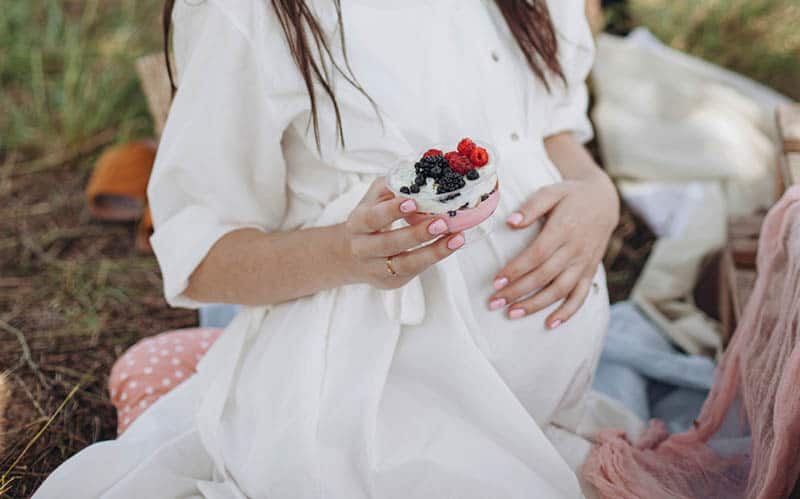 pregnant woman holding a berry dessert on a picnic