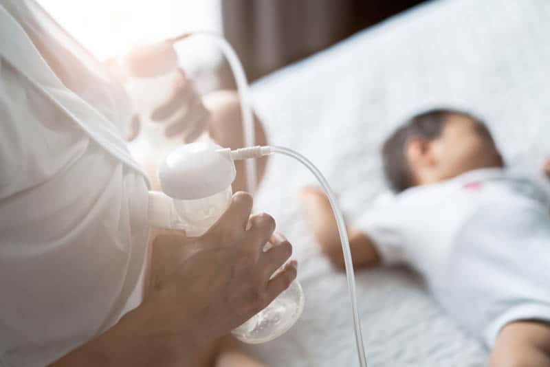 woman pumping breast milk with two pumps while baby sleeping