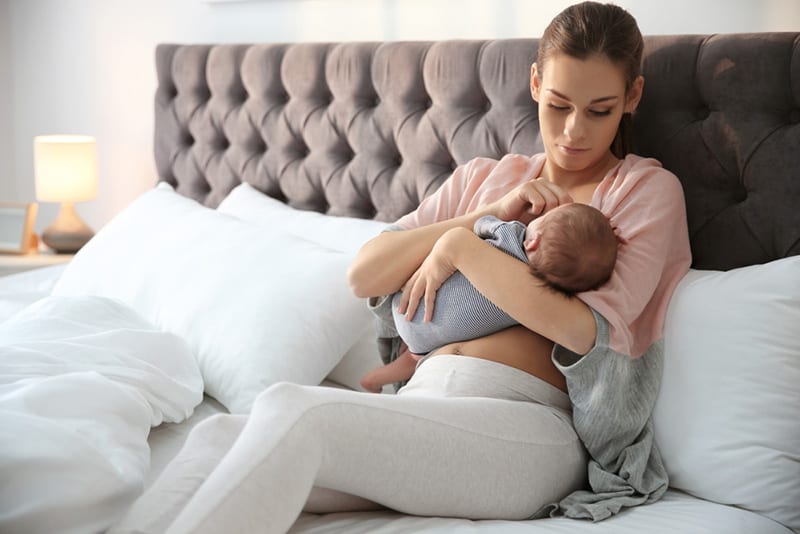 young woman breastfeeding her baby in bedroom