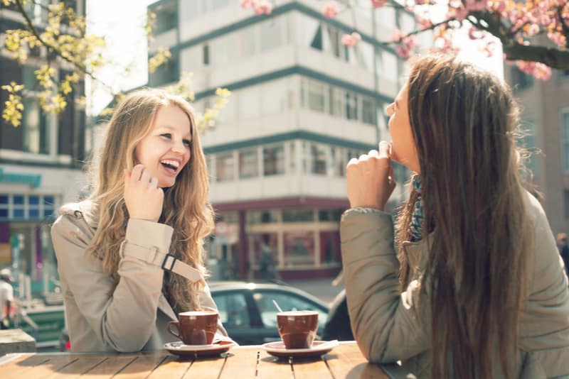 två unga kvinnor pratar och dricker kaffe i cafe