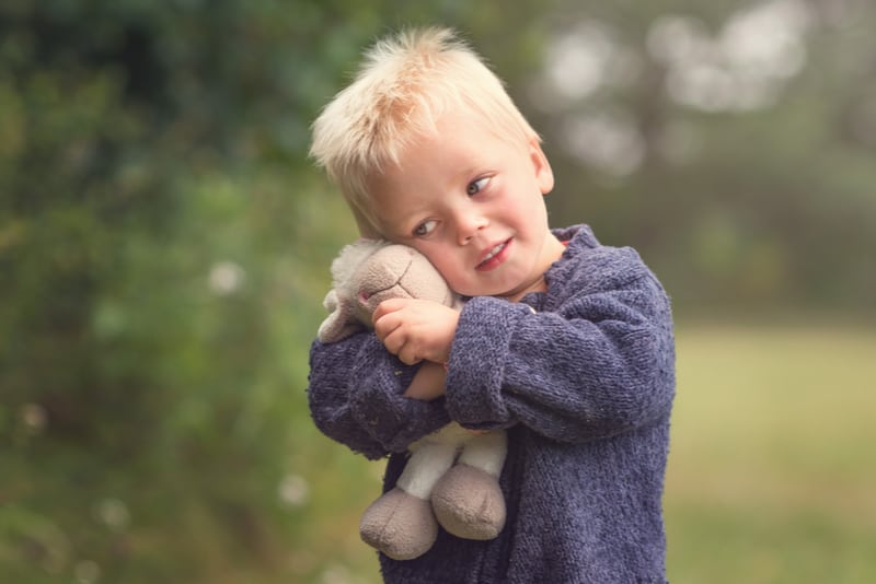 blond boy holding plush sheep in the park