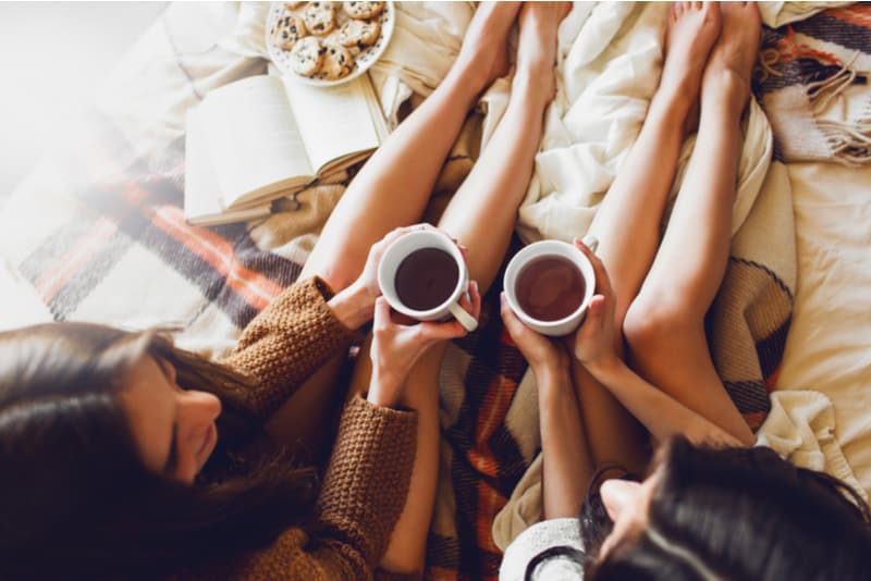 duas irmãs na cama com livros antigos e uma xícara de chá nas mãos