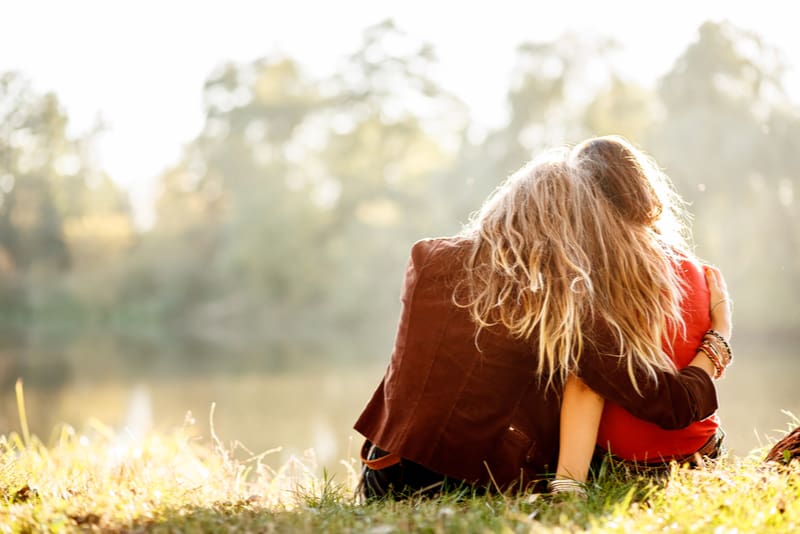 dos mujeres jóvenes sentadas en el césped abrazándose