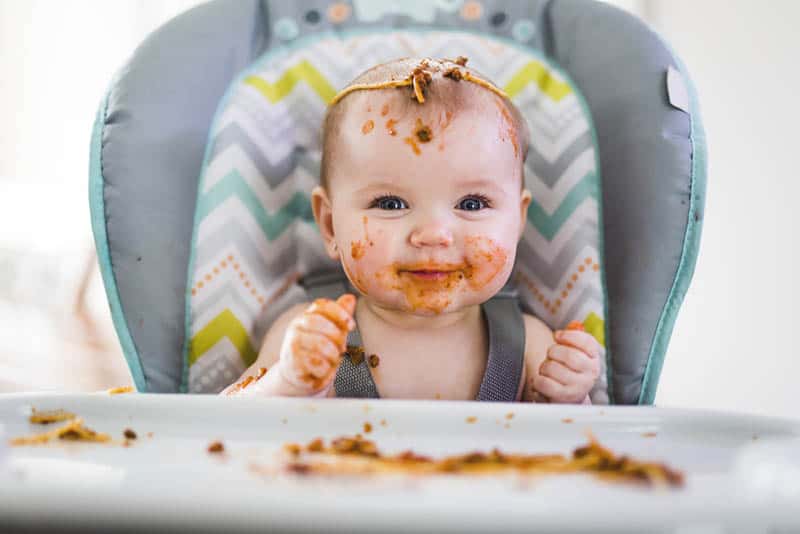 cute baby covered with food in the high chair