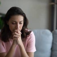 young woman sitting anxiously on the couch with her hands clasped together