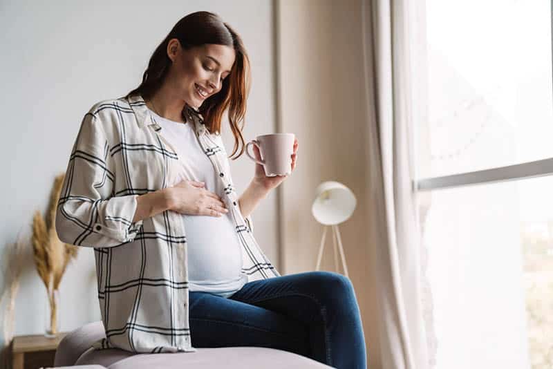 happy pregnant woman drinking coffee and smiling to her belly