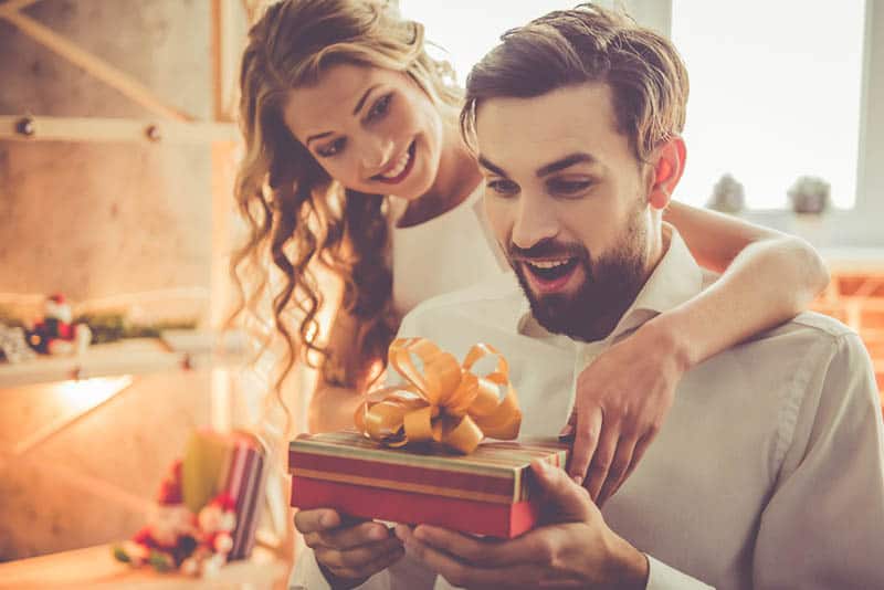 happy woman surprising her husband with birthday gift