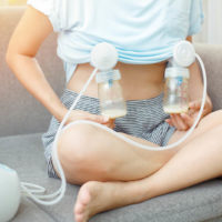 young woman using breast pump to express milk on the couch