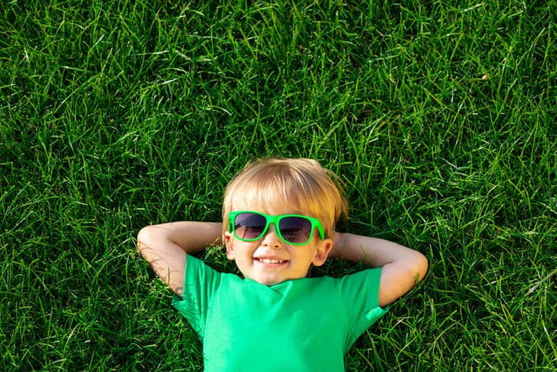 Happy child wearing green sunglasses lying in grass