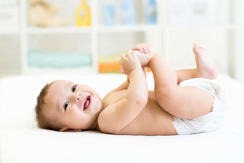 cute baby boy wearing only diapers lying on back and smiling