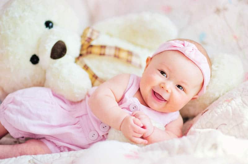 cute baby girl smiling on the bed with teddy bear toy