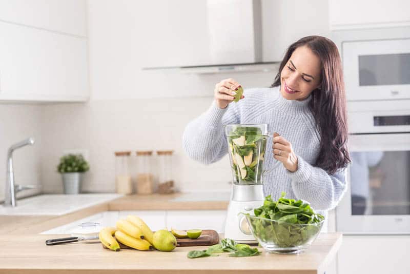 smiling woman preparing smoothie in the kitchen