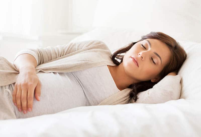young pregnant woman dreaming while sleeping in bed